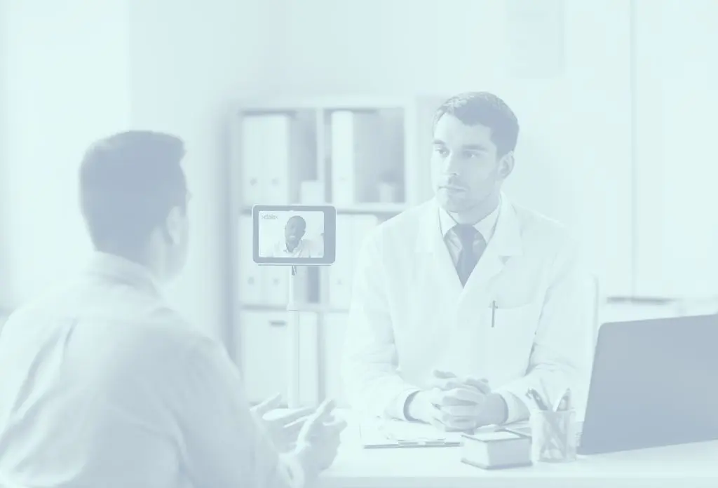 A doctor consults with a patient in an office while another doctor joins via video call on a tablet.